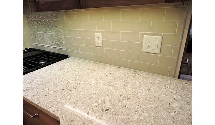 Remodeled kitchen with green bricks on the walls and with white granite countertops