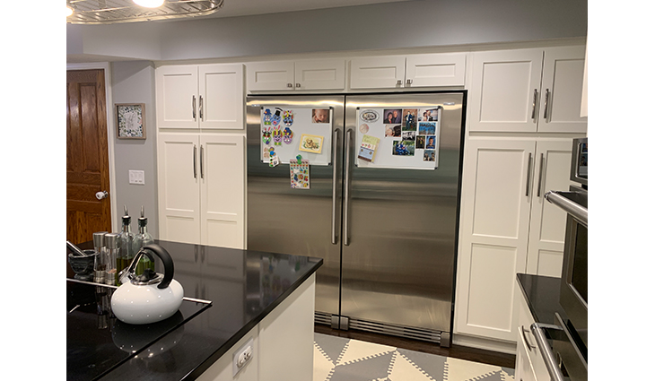 Double-wide fridge surrounding by wall to wall cabinets