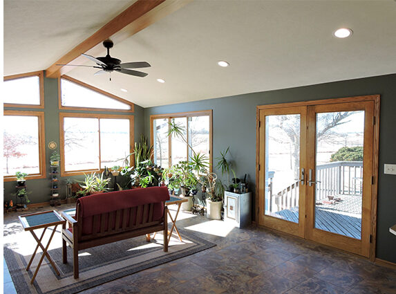 Sunroom addition with vaulted ceiling, recessed lighting, tile floors, and wood-grain window frames.