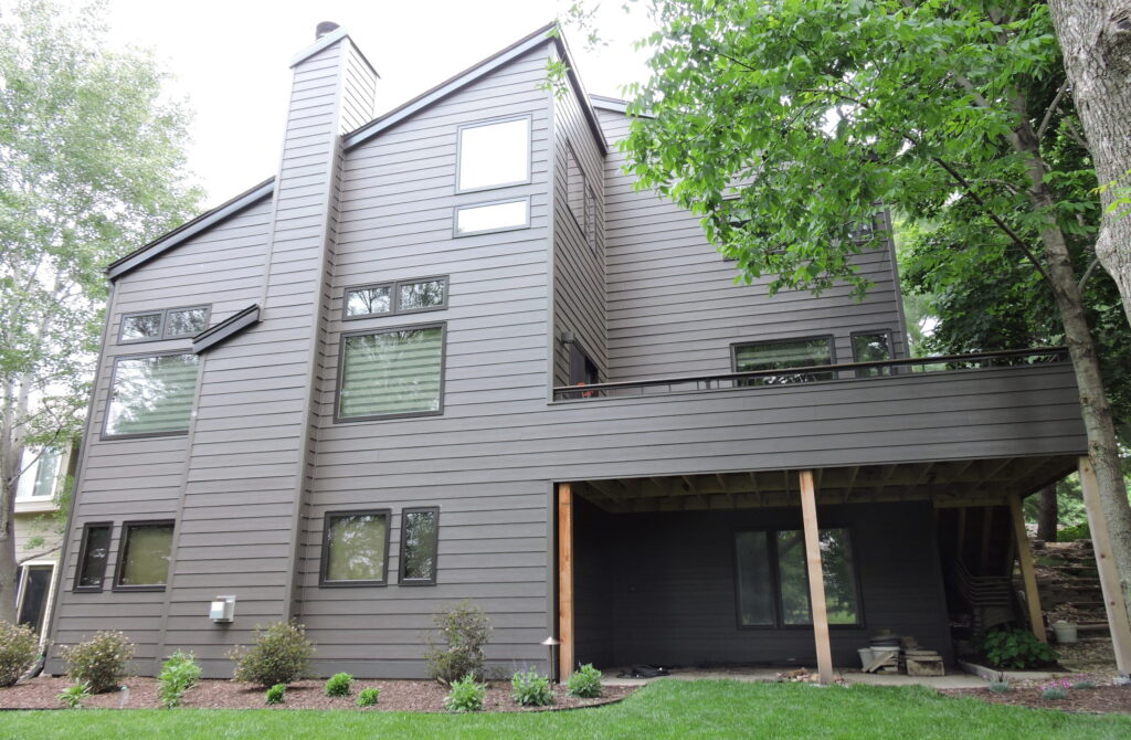 Exterior dark gray siding on a two-story house with trees on either side.