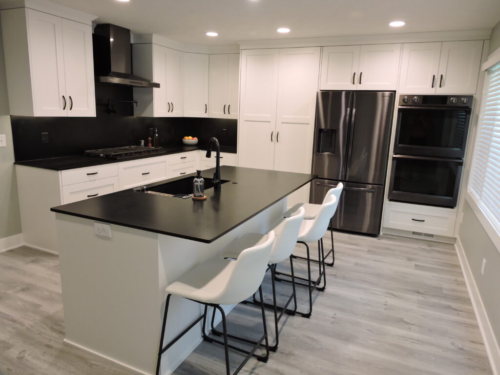 Remodeled kitchen with black countertops, black backsplash, white cabinets, large island, and recessed lighting.