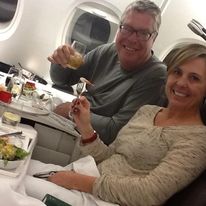 Two people sitting together on an airplane, with meals and drinks on trays in front of them.