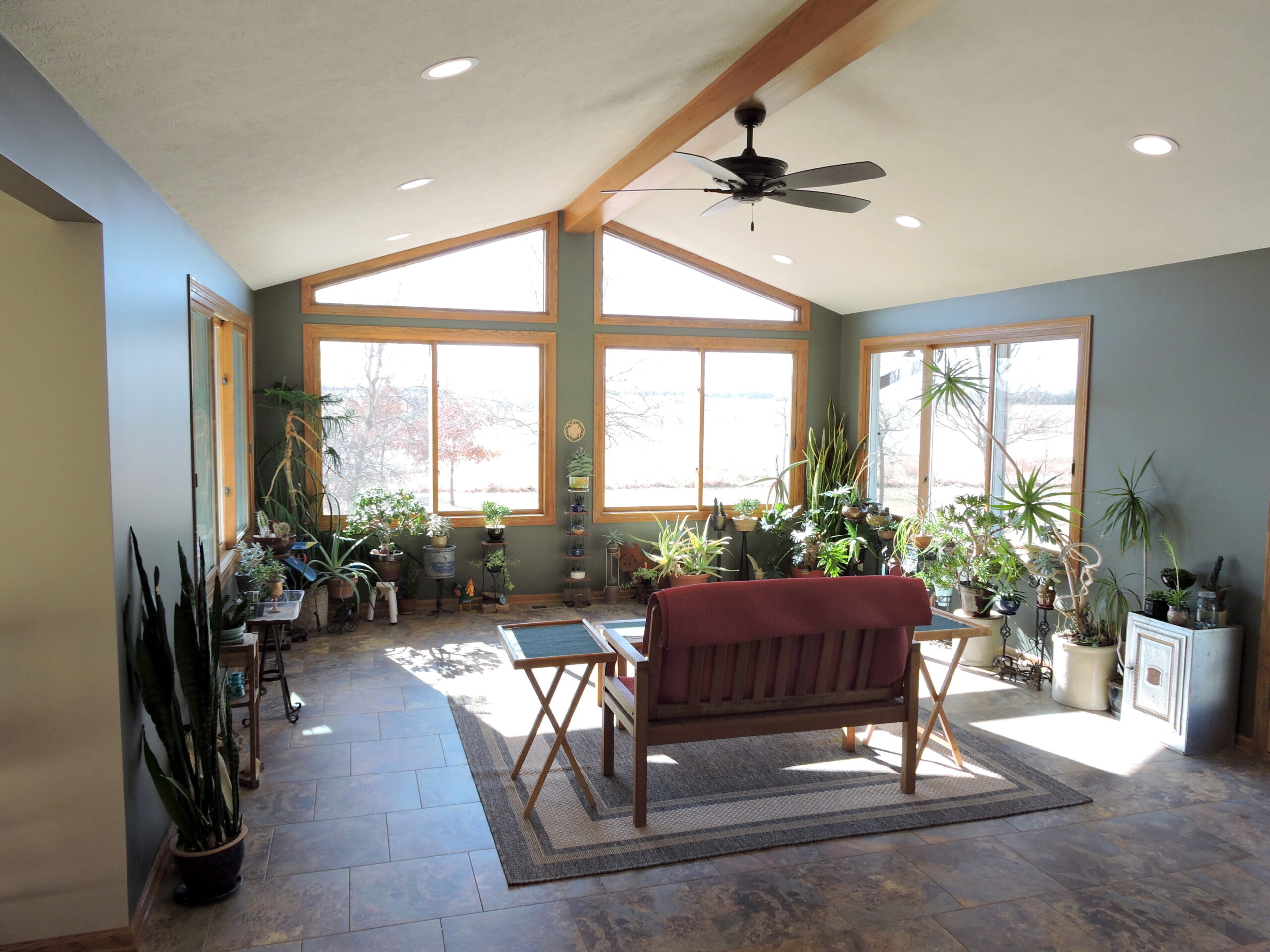 Sunroom addition with large windows and a ceiling fan. The walls are lined with plants.