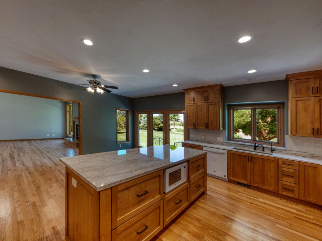 Remodeled kitchen with wood floors and cabinetry, stone countertops, recessed lighting, dark walls.
