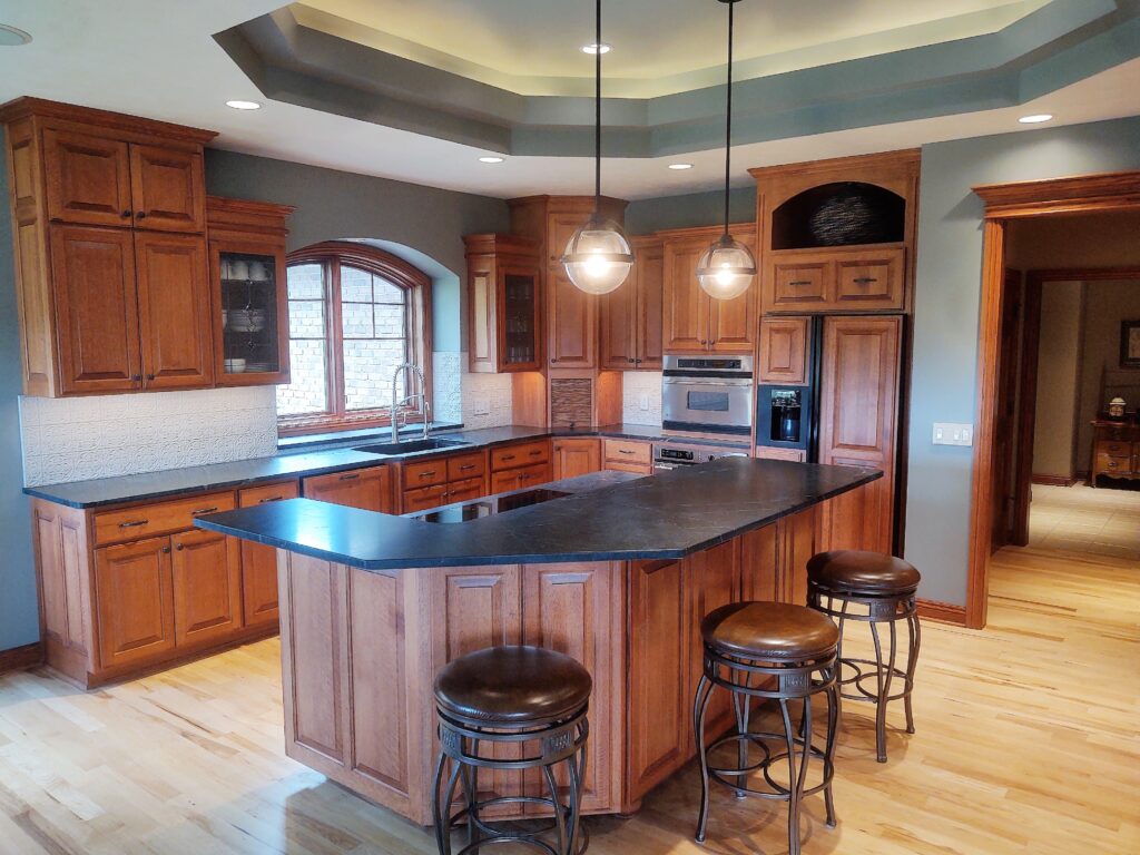Remodeled kitchen with large island, wood cabinetry, recessed lighting, 2 pendant lights over the island, and dark countertops. 