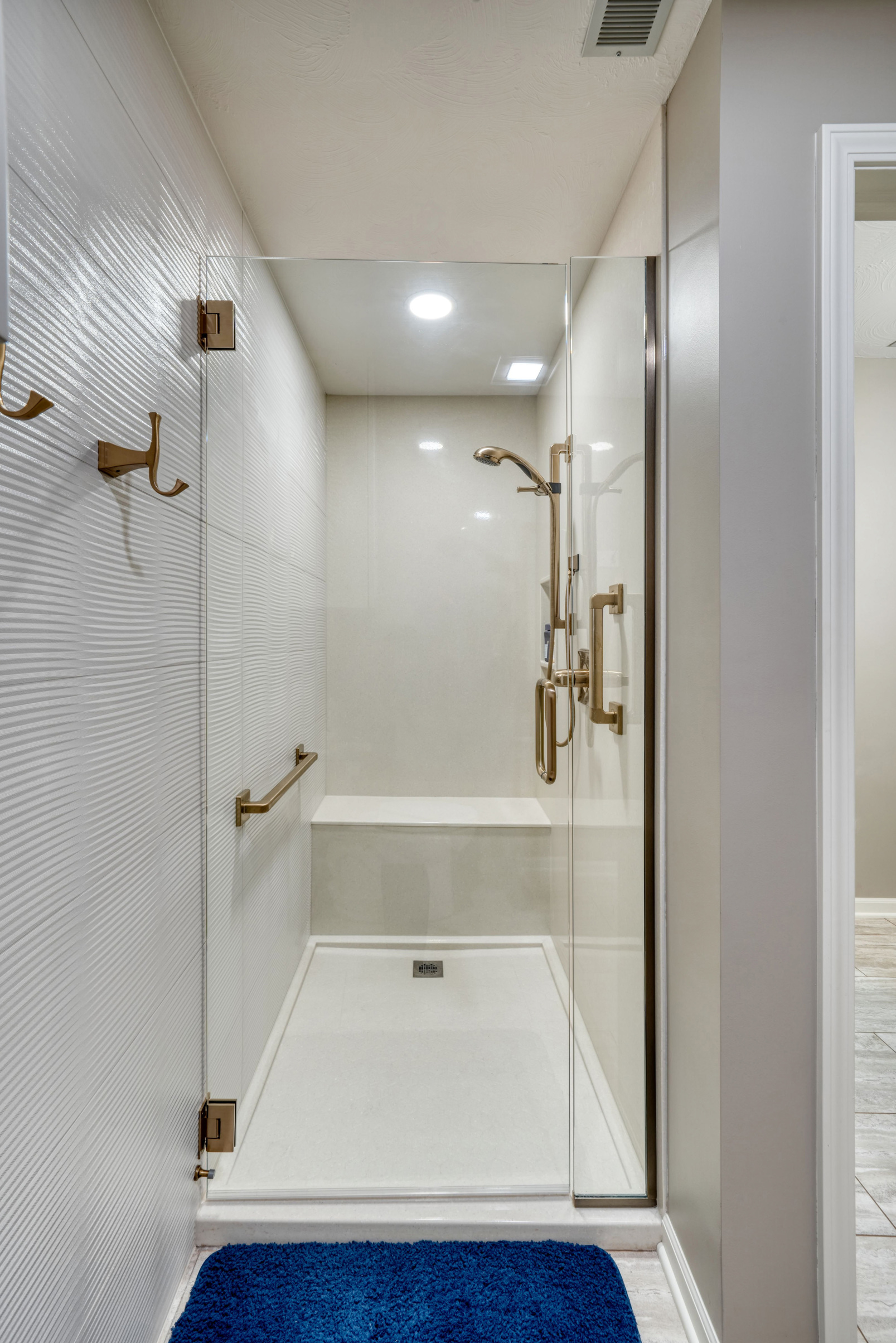 Remodeled bathroom with stand-in shower with built-in seating and grab bar.