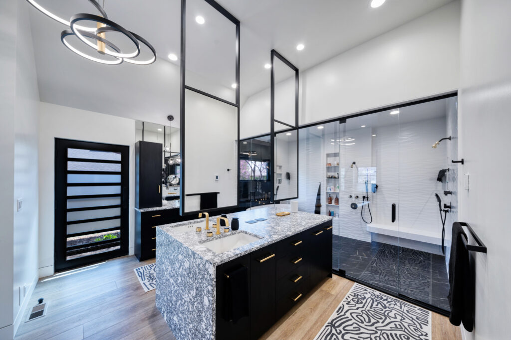 Large bathroom remodel with black cabinets, gray stone waterfall countertop, black-framed mirrors, and glass-enclosed shower.