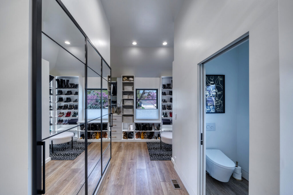 Large walk-in closet with recessed lighting, custom shelving, and wood floors. Wall of mirrors on the left.