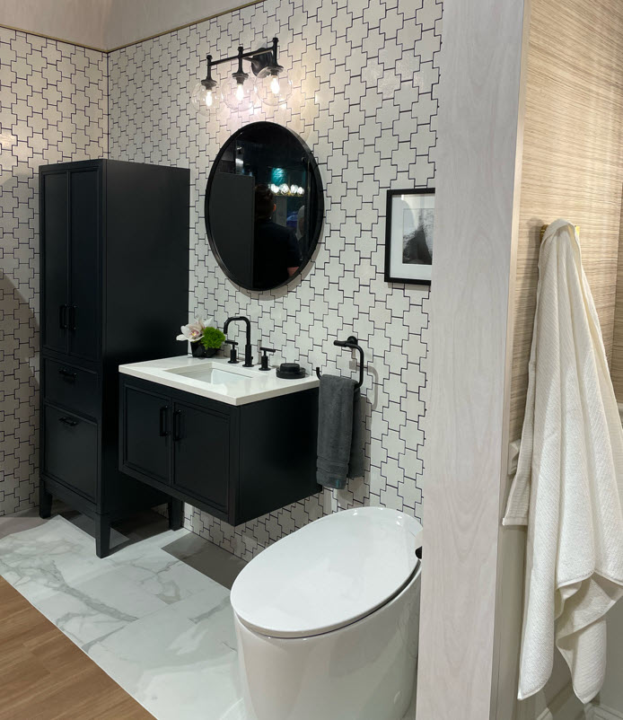 Remodeled small bathroom with floating black vanity, round black-framed mirror, and tall black cabinet. Modern toilet and vanity light. White tile walls.