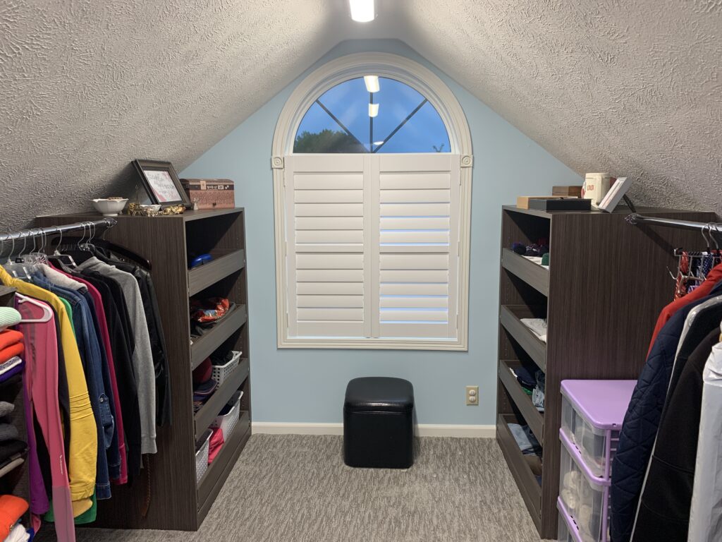 a closet with slanted ceilings, and a round-top window in the back