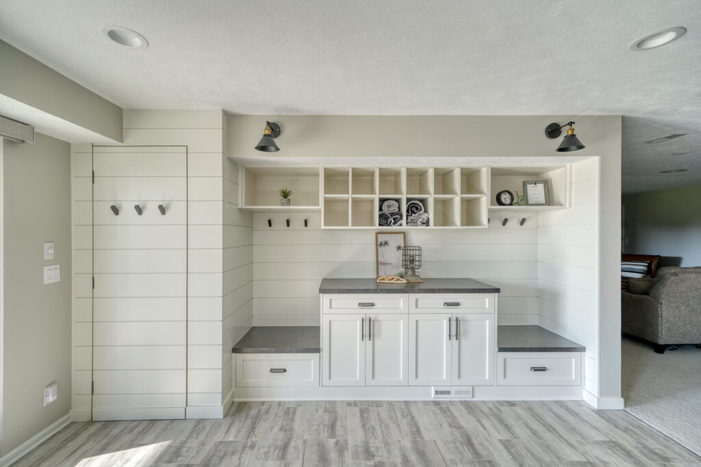 Mudroom addition with white shiplap wall, built-in white storage and benches, light gray wood-look flooring, recessed lights.