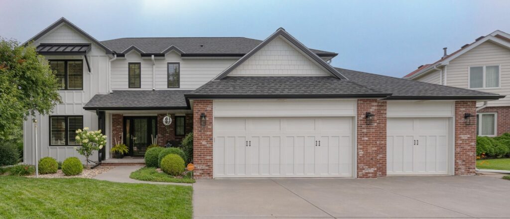 Exterior of modern home with gray/white siding and two white garage doors with brick surround.