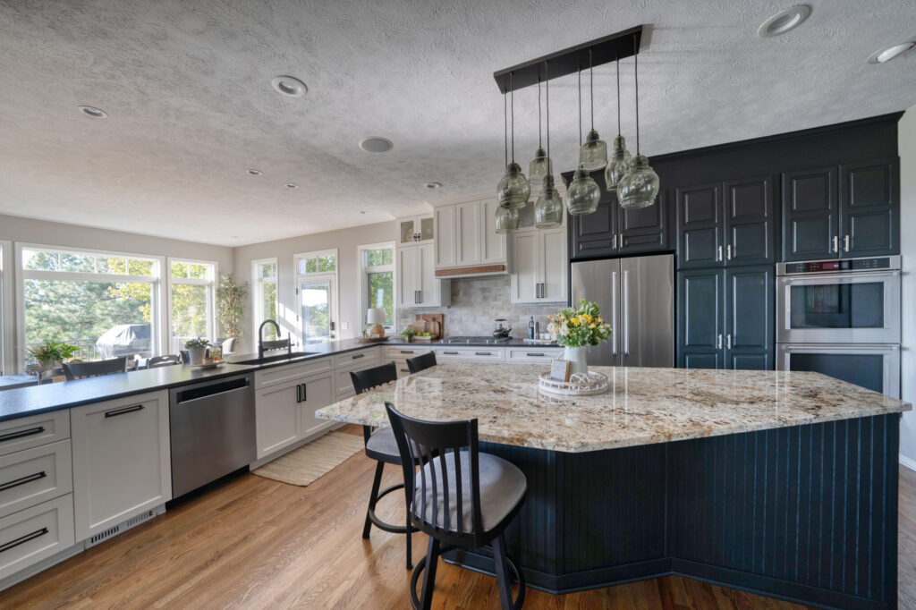 Kitchen with marble counters and white and dark cabinets. Row of windows along left wall. Large island. Wood floors.