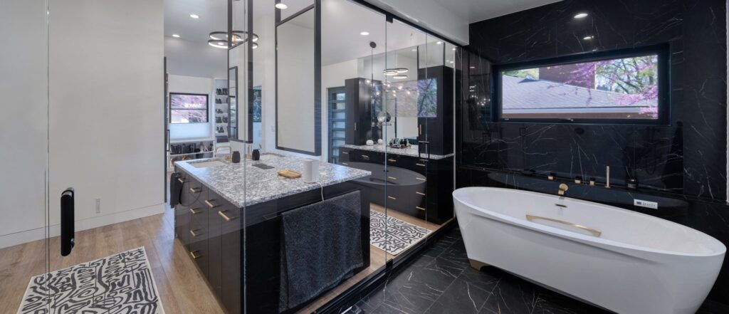 Remodeled bathroom with glass walls, soaking tub, and large vanity. Black cabinets and black marble tile in shower area.