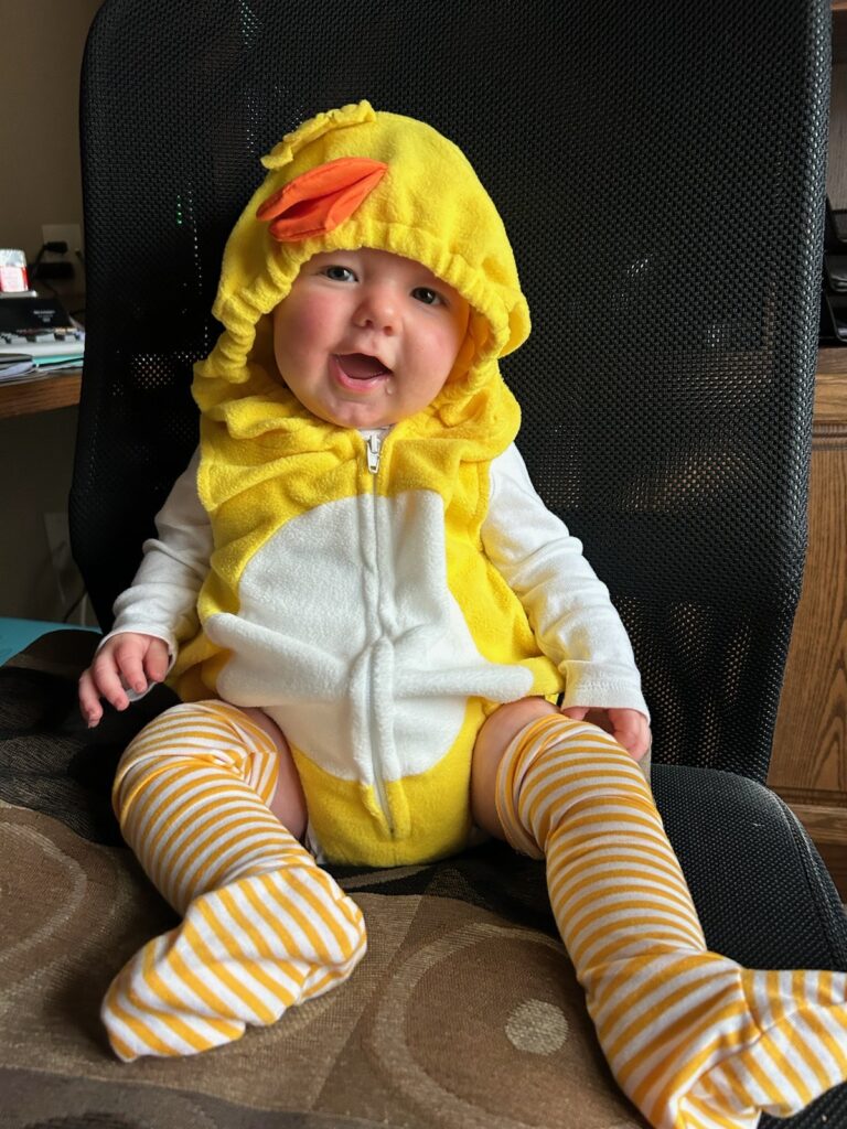 Baby Vincent sitting on a chair, smiling and wearing a duck outfit.