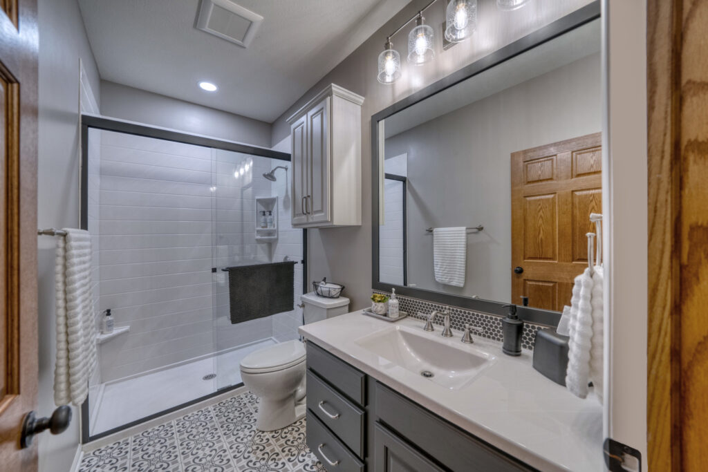 Remodeling bathroom with large mirror and walk-in shower. Gray vanity with white countertop.