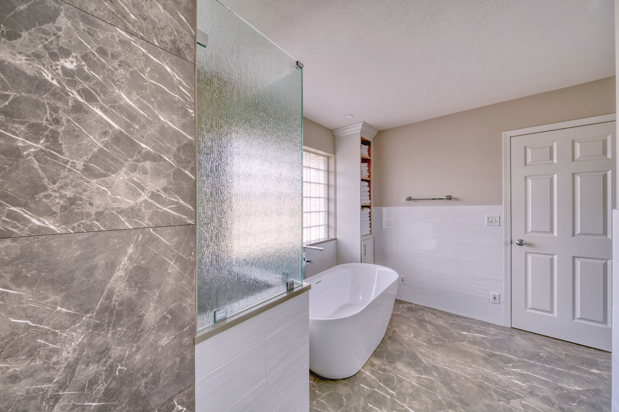 Remodeled bathroom with freestanding tub and walk-in shower. Gray tile floor, white tile on far wall.