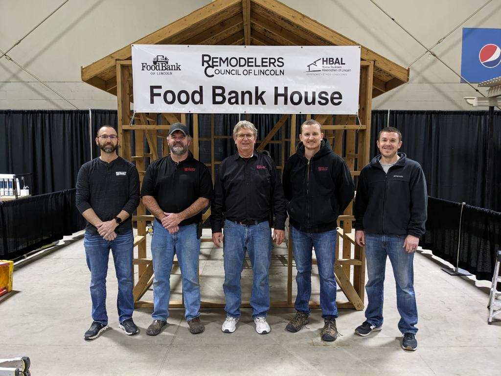 Five men from the Willet team lined up under a Food Bank House sign