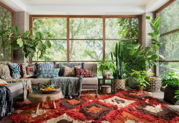 A living room with Boho-style decor, including bright red shag rug and lots of plants, in a room with large floor-to-ceiling windows.