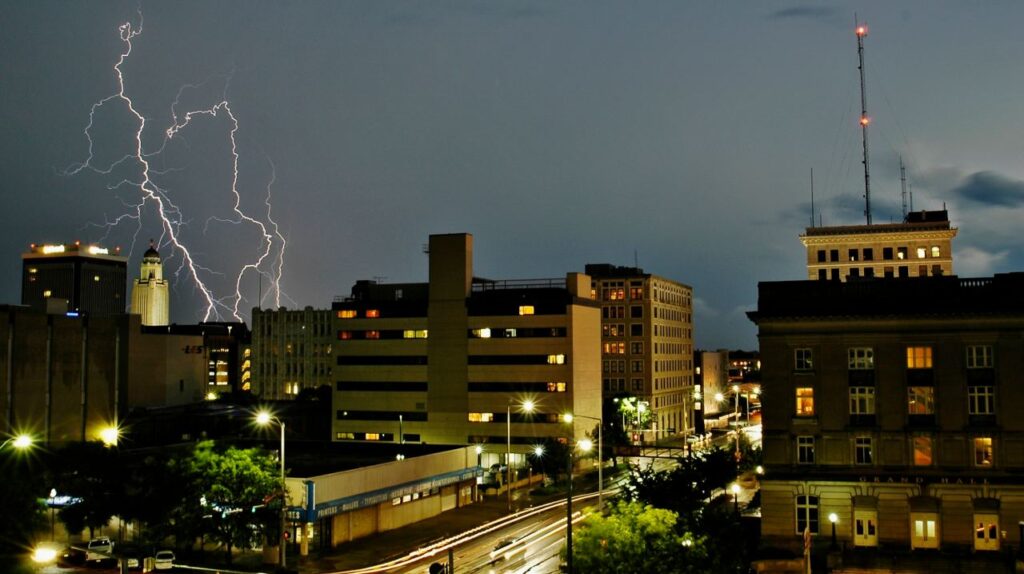 View of a city with large buildings, dark sky, and lightning bolts off to the left.