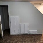 Image of carpeted basement area with white wall along stairs and closet open under stairs.