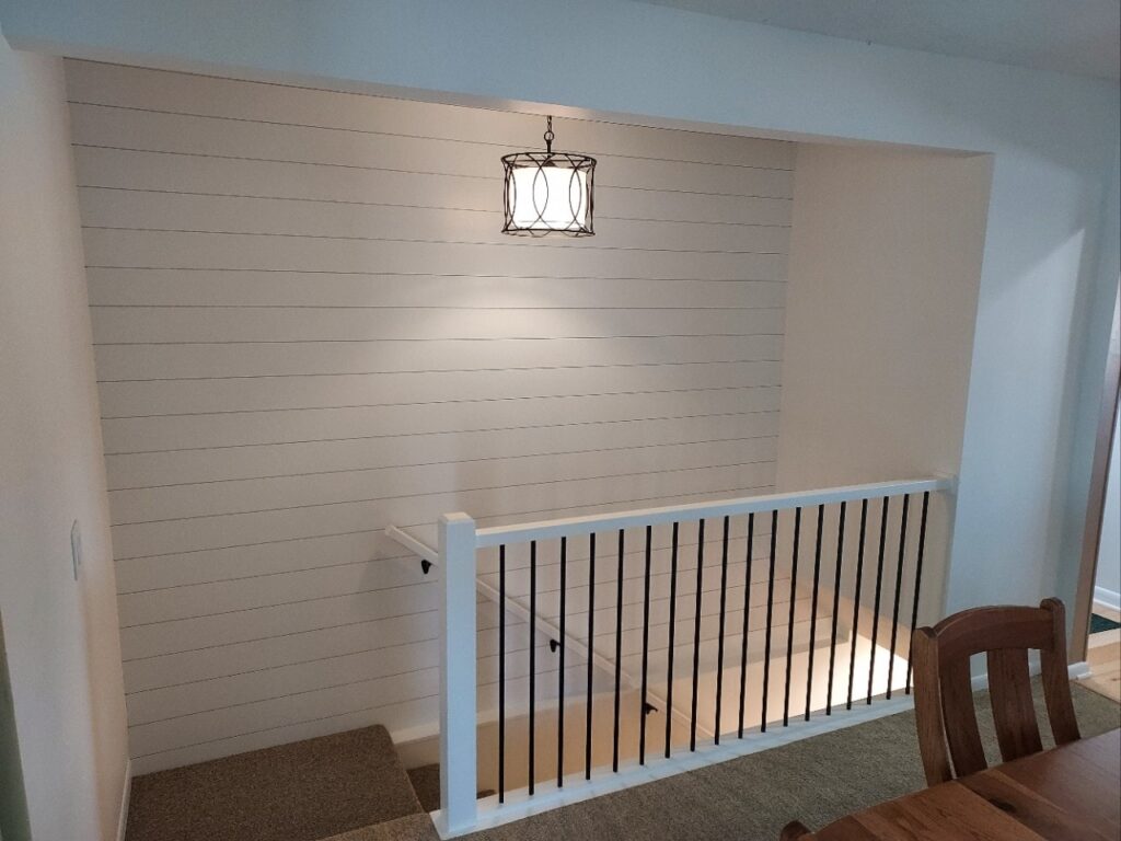 Updated stair railing and white shiplap wall and black metal light fixture in stairwell.