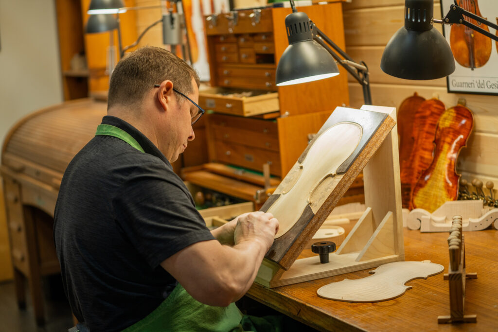 An image of a workshop being used. A man is making instrument frames at a desk.