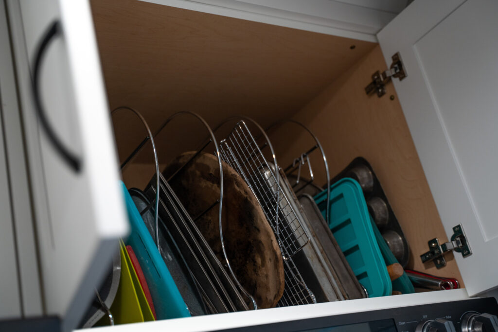 A kitchen cabinet with metal organizers in it. A lot of pans and racks are seen in the organizer
